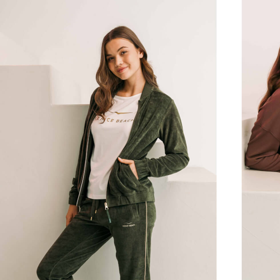 Frau in dunkelgrünem Jogginganzug und weißem T-Shirt mit goldenem Venice Beach Logo.