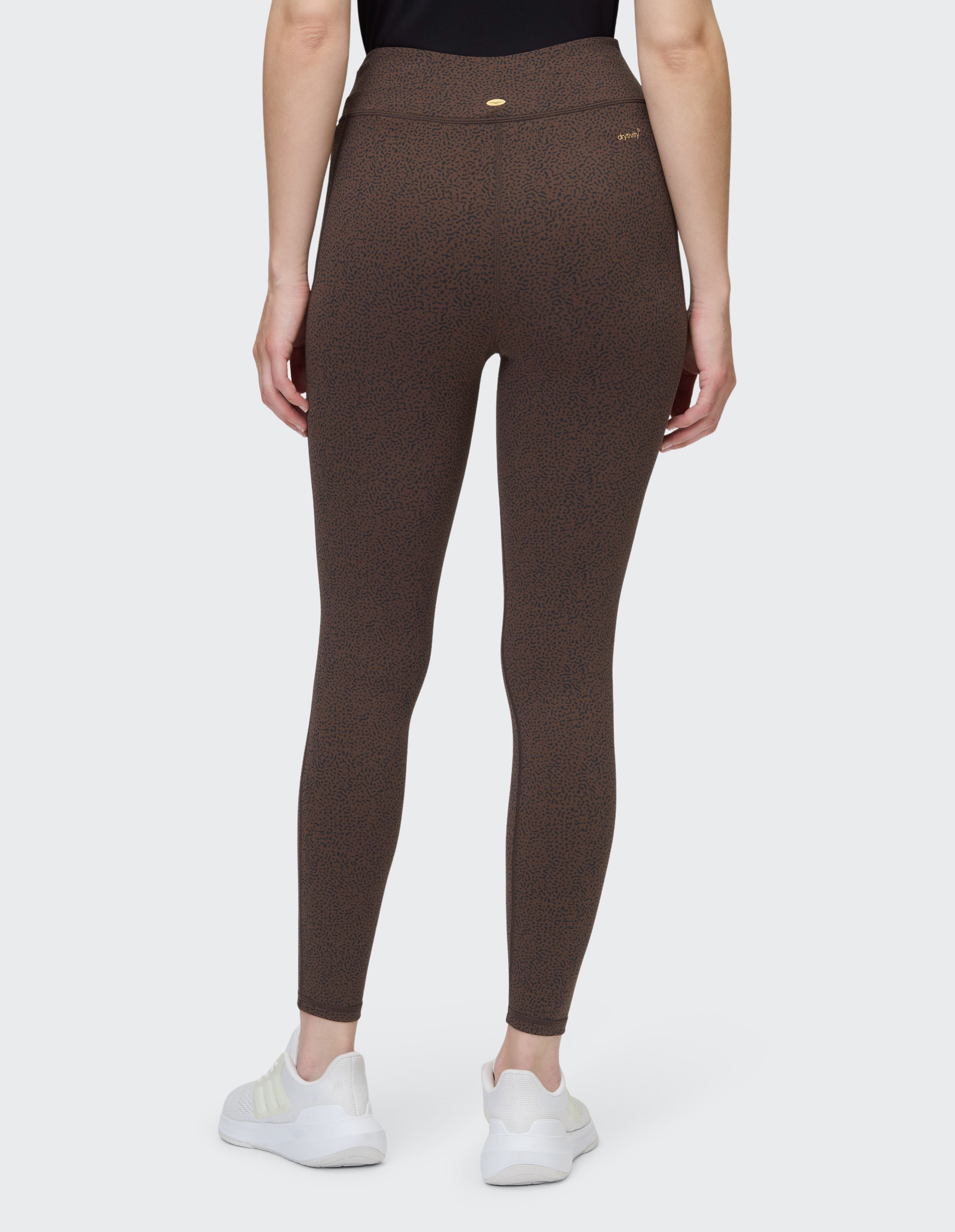 Eine Person trägt braune Leggings mit feinem Muster, weiße Turnschuhe und ein schwarzes Oberteil, von hinten gesehen.