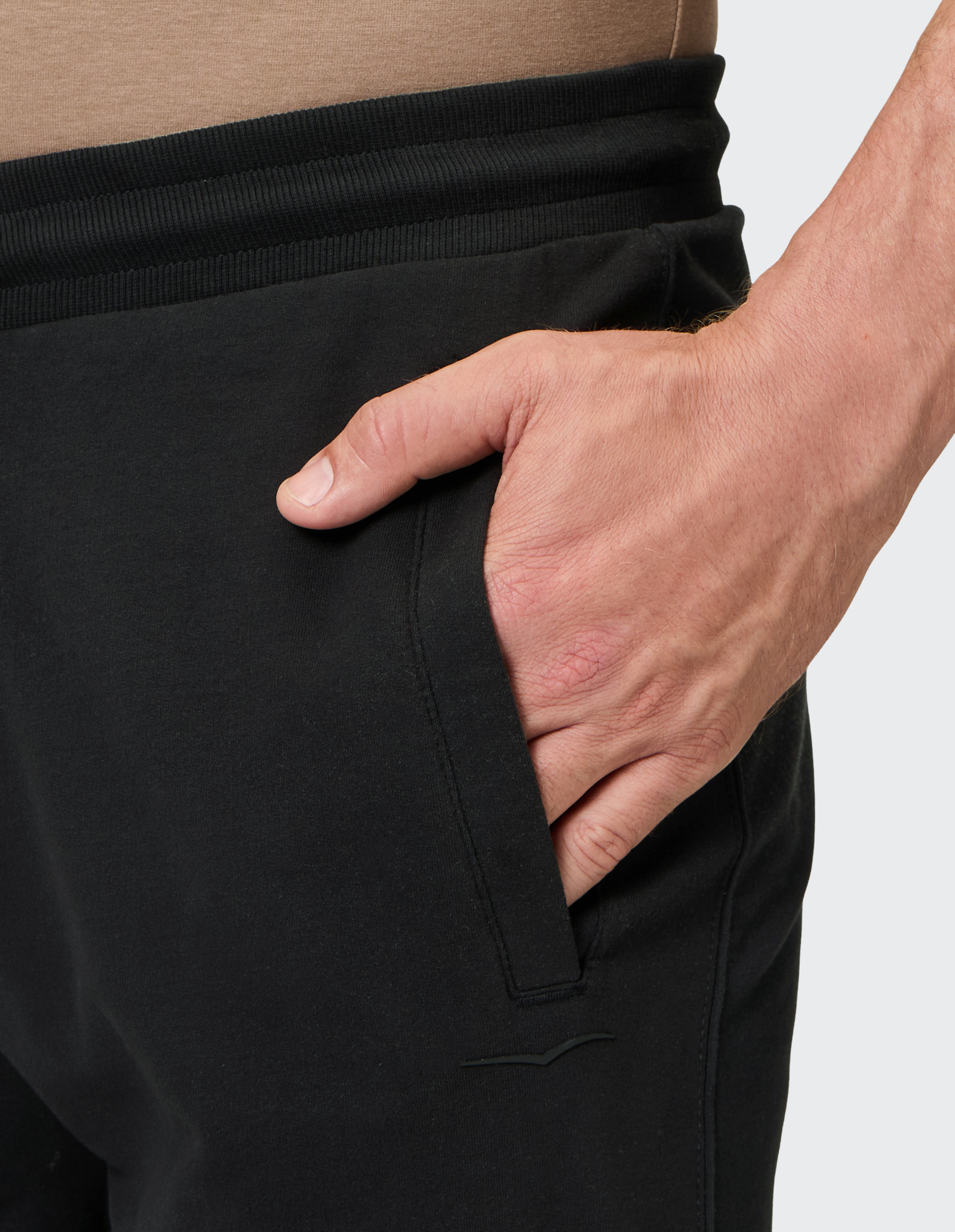 Nahaufnahme einer Hand in der Tasche einer schwarzen Hose mit elastischem Bund, getragen mit einem beigen Oberteil.