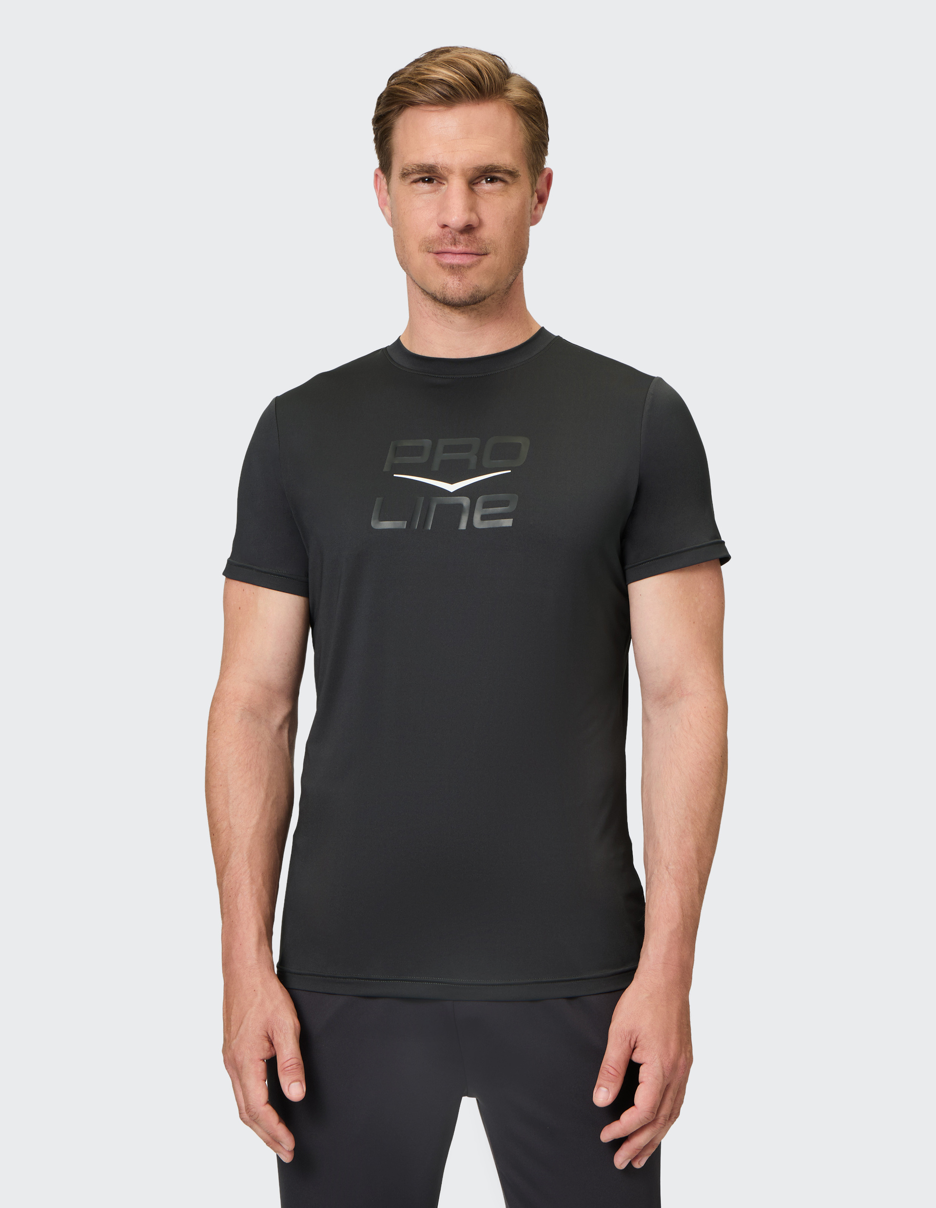 Mann in schwarzem T-Shirt mit der Aufschrift "Pro Line", blickt freundlich in die Kamera; hellgrauer Hintergrund.