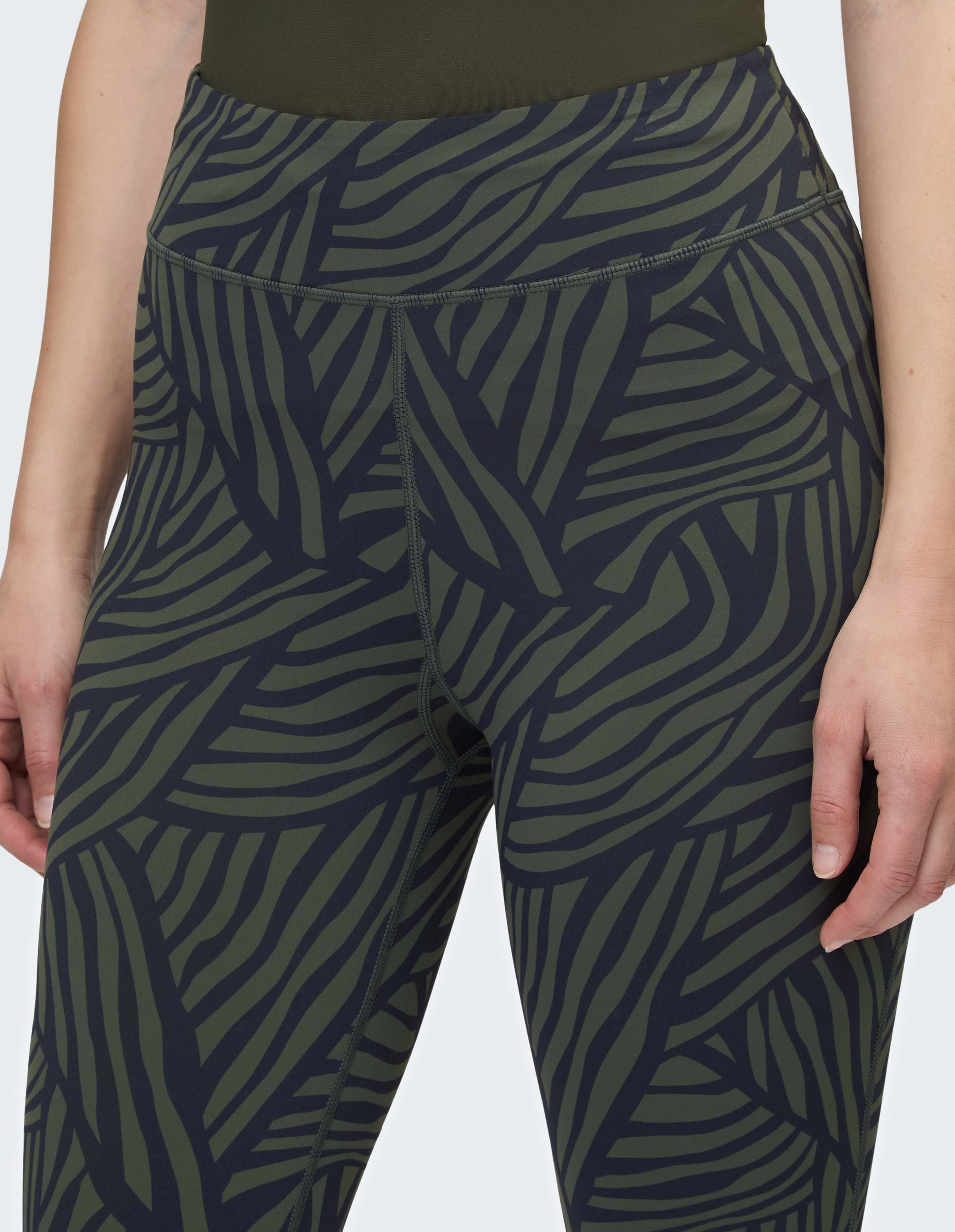 Nahaufnahme von grüner Sportleggings mit dunkelblauem, blattähnlichem Muster, getragen von Person mit teilweise sichtbarer Hand.