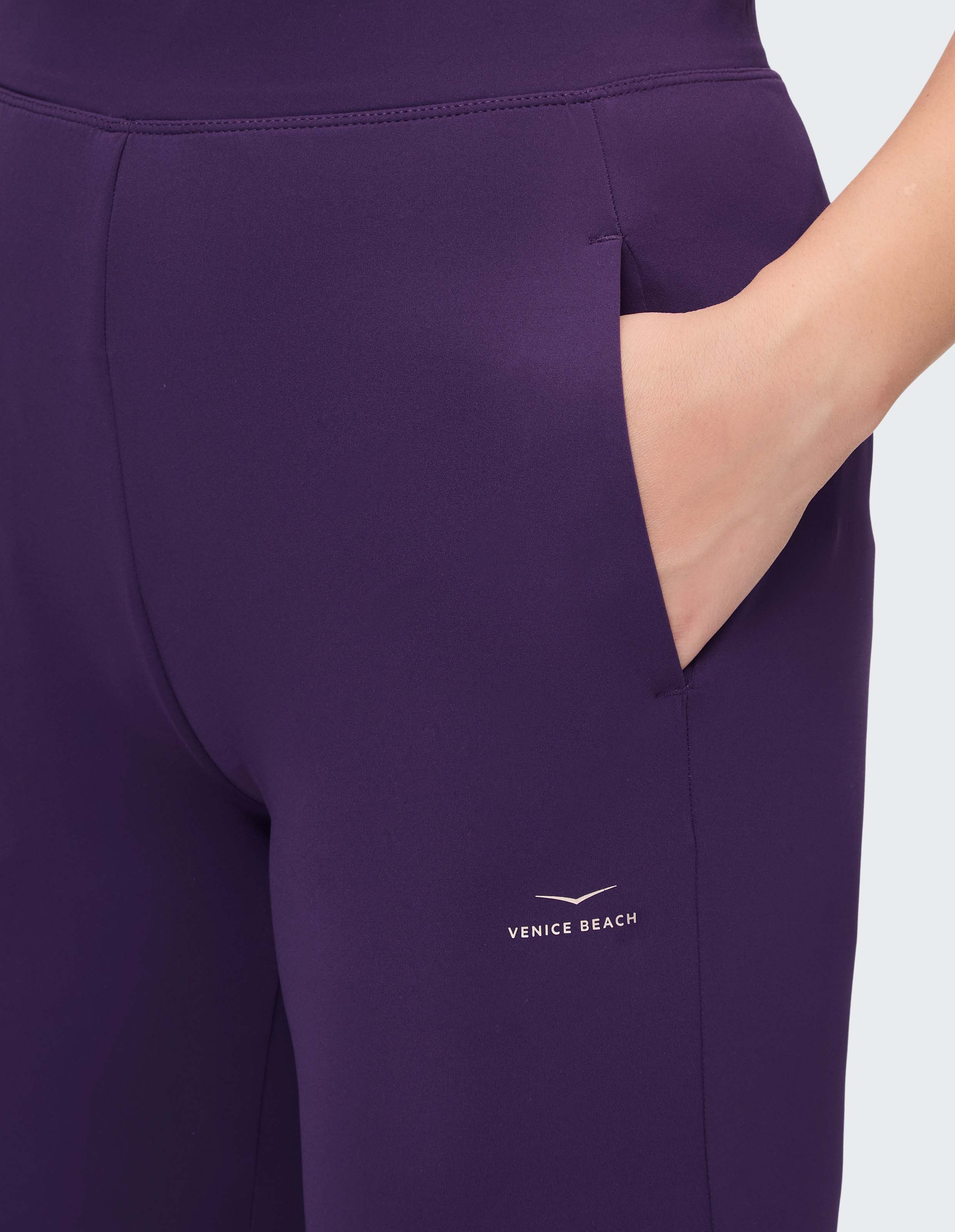 Lila Sportleggings mit eingesteckter Hand in der rechten Tasche, verziert mit dem Logo "Venice Beach" über dem Knie.