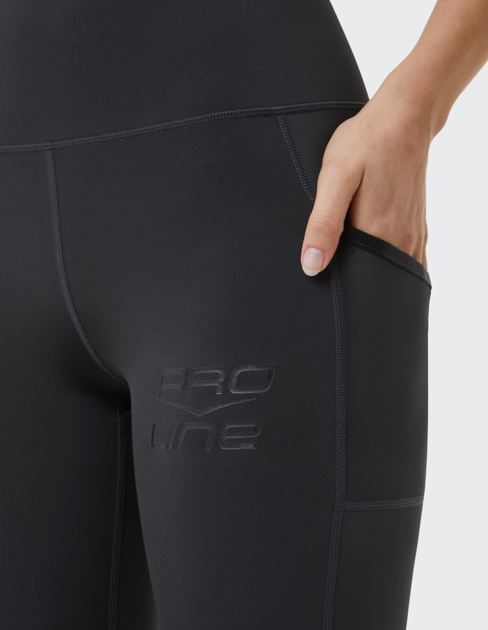 Nahaufnahme einer schwarzen Sportleggings mit der Aufschrift "Pro Line", eine Hand greift in die seitliche Netztasche.