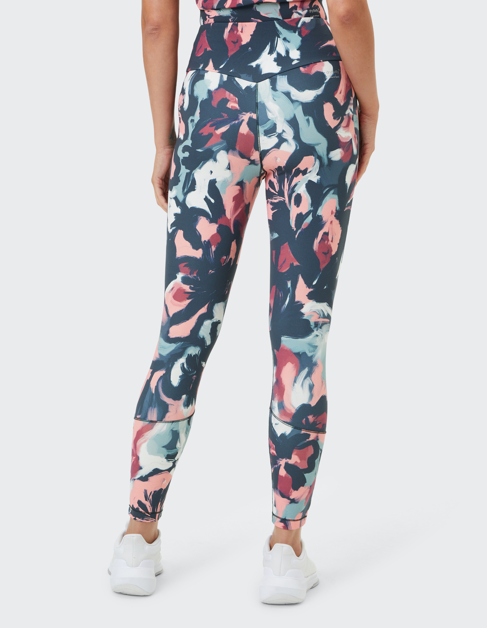Frau in bunter Leggings mit abstraktem Blumenmuster in Rosa, Blau und Weiß, von hinten, trägt weiße Sneakers.