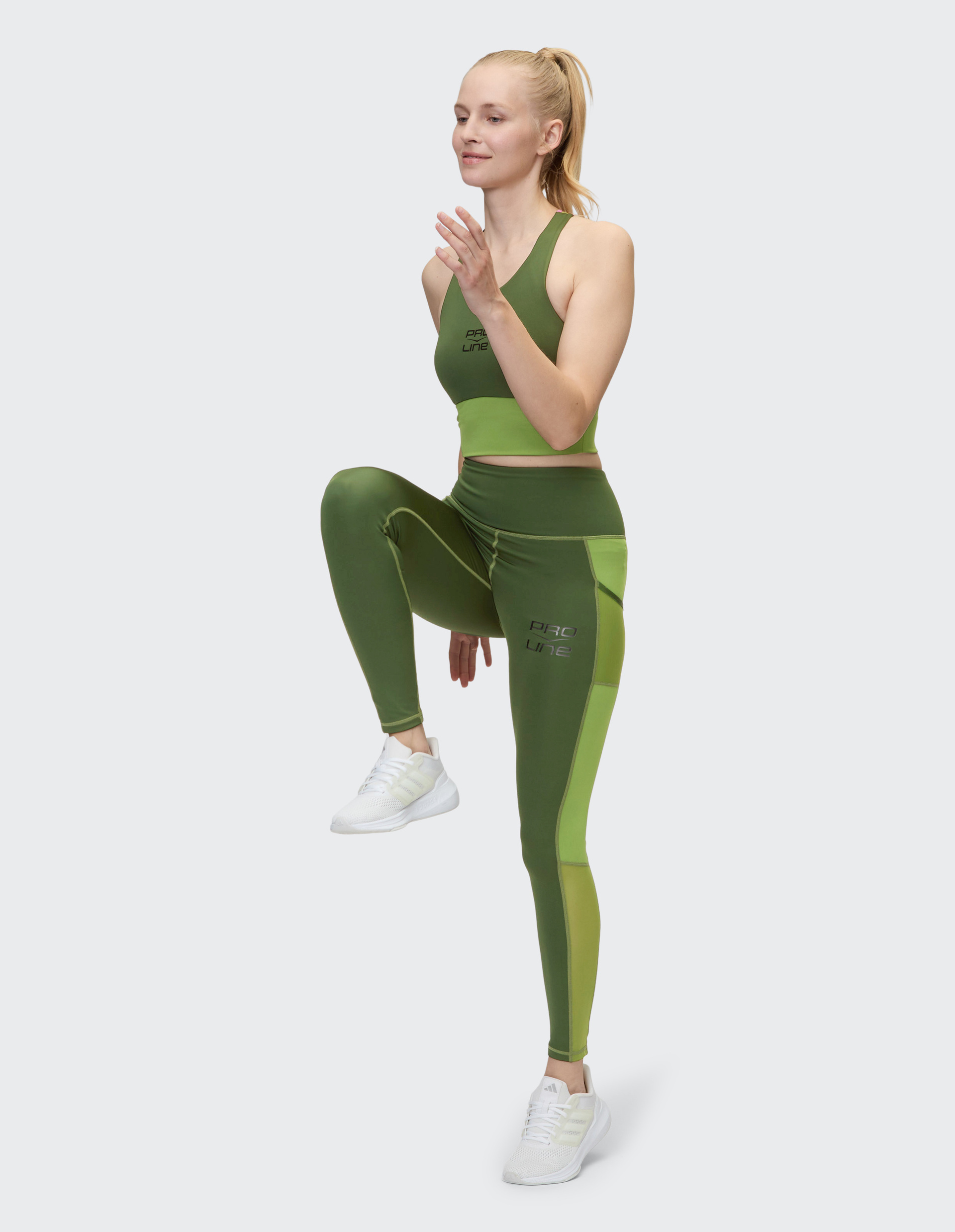 Eine Frau in grüner Sportkleidung joggt an Ort und Stelle, das linke Knie angehoben, der Blick entspannt nach vorne.