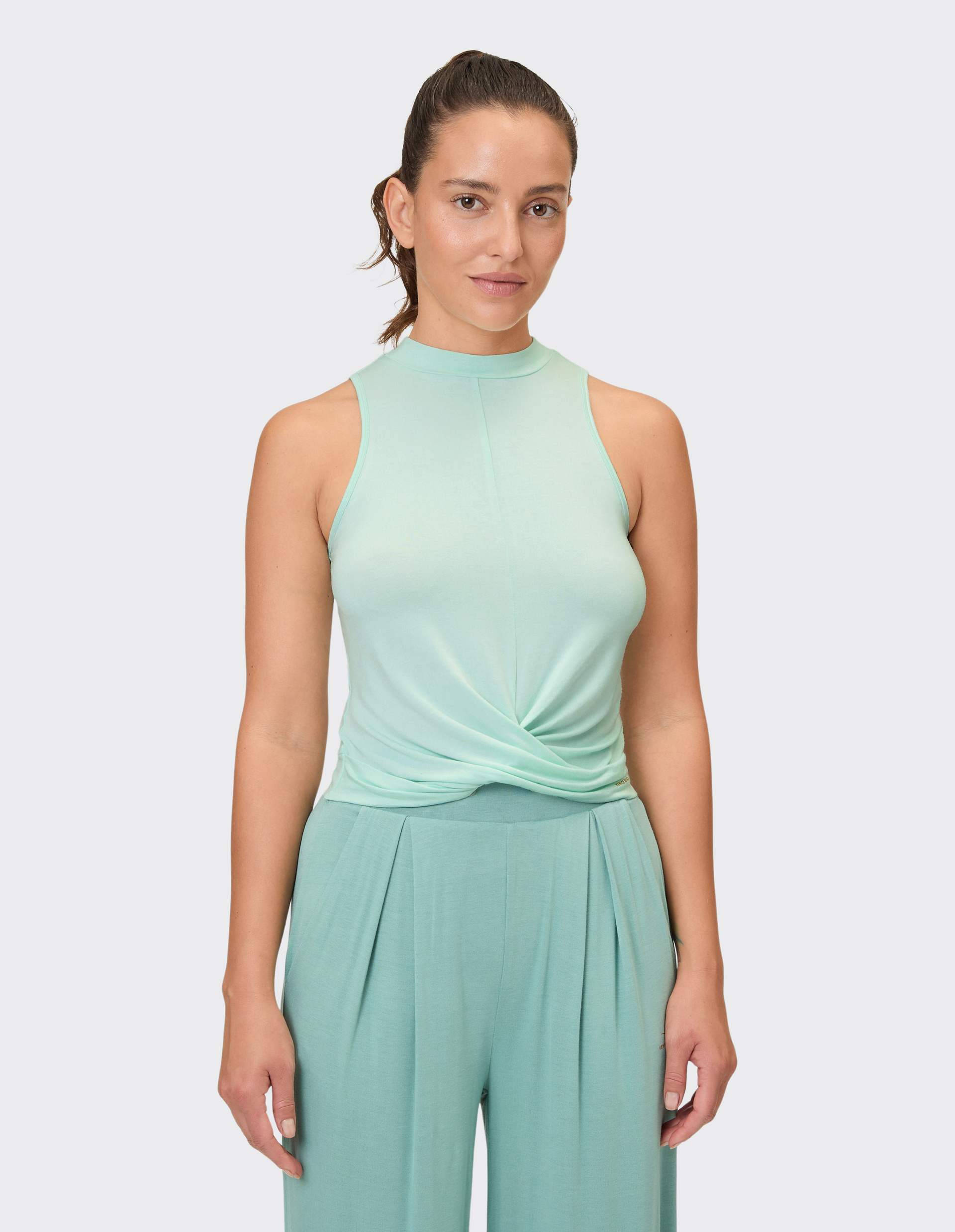 Eine Frau trägt ein mintgrünes, ärmelloses Oberteil mit verdrehtem Vordenteil und dazu passende weite Hosen mit Falten.