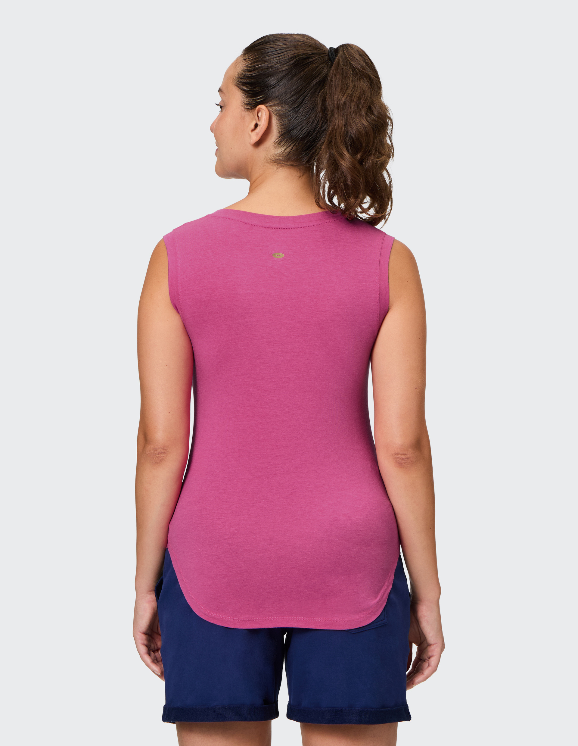 Frau von hinten in pinkem ärmellosen Shirt und dunkelblauer Shorts, trägt einen Pferdeschwanz, vor hellem Hintergrund.