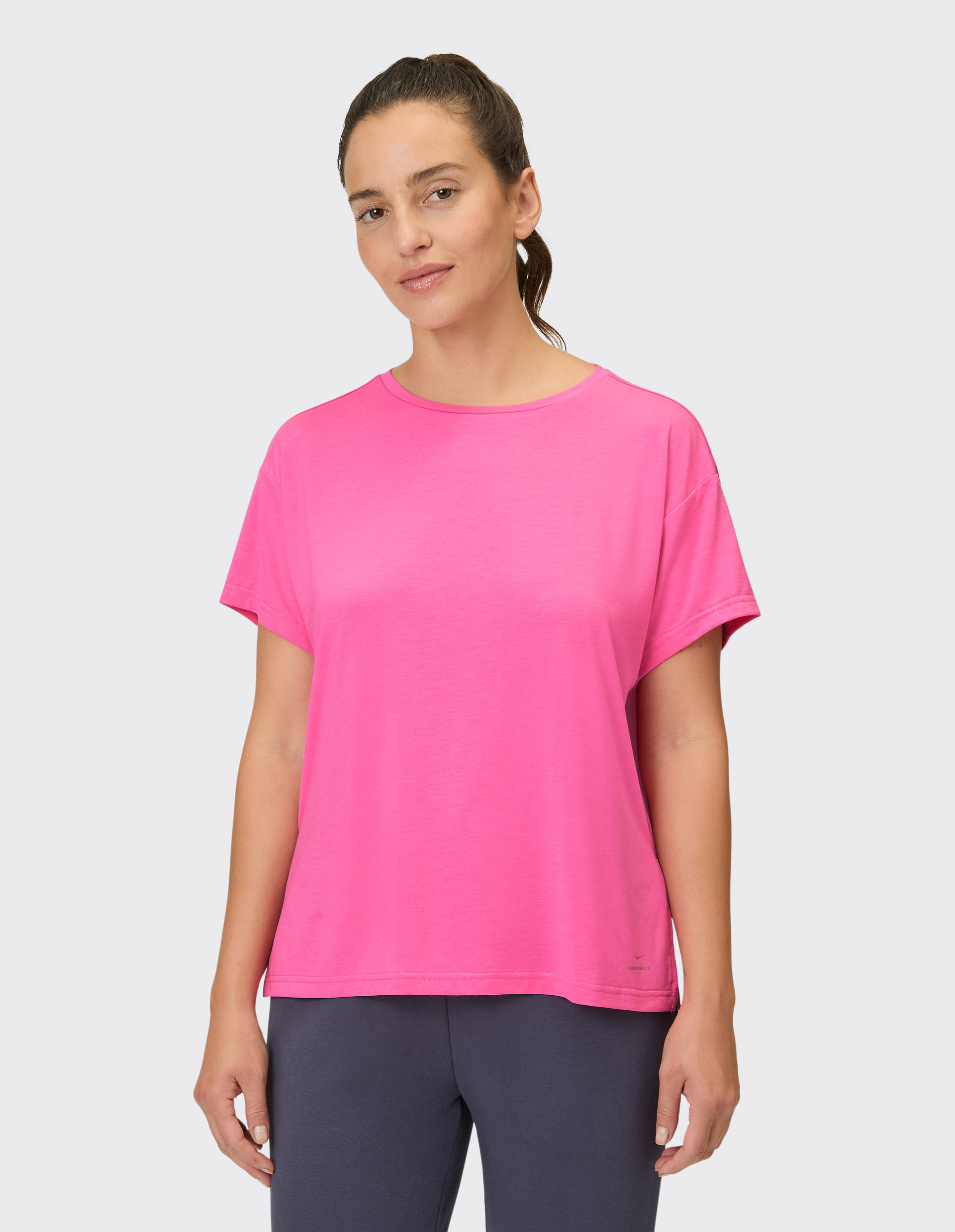 Eine Frau trägt ein leuchtend pinkes T-Shirt mit kurzen Ärmeln und eine dunkelblaue Hose.
