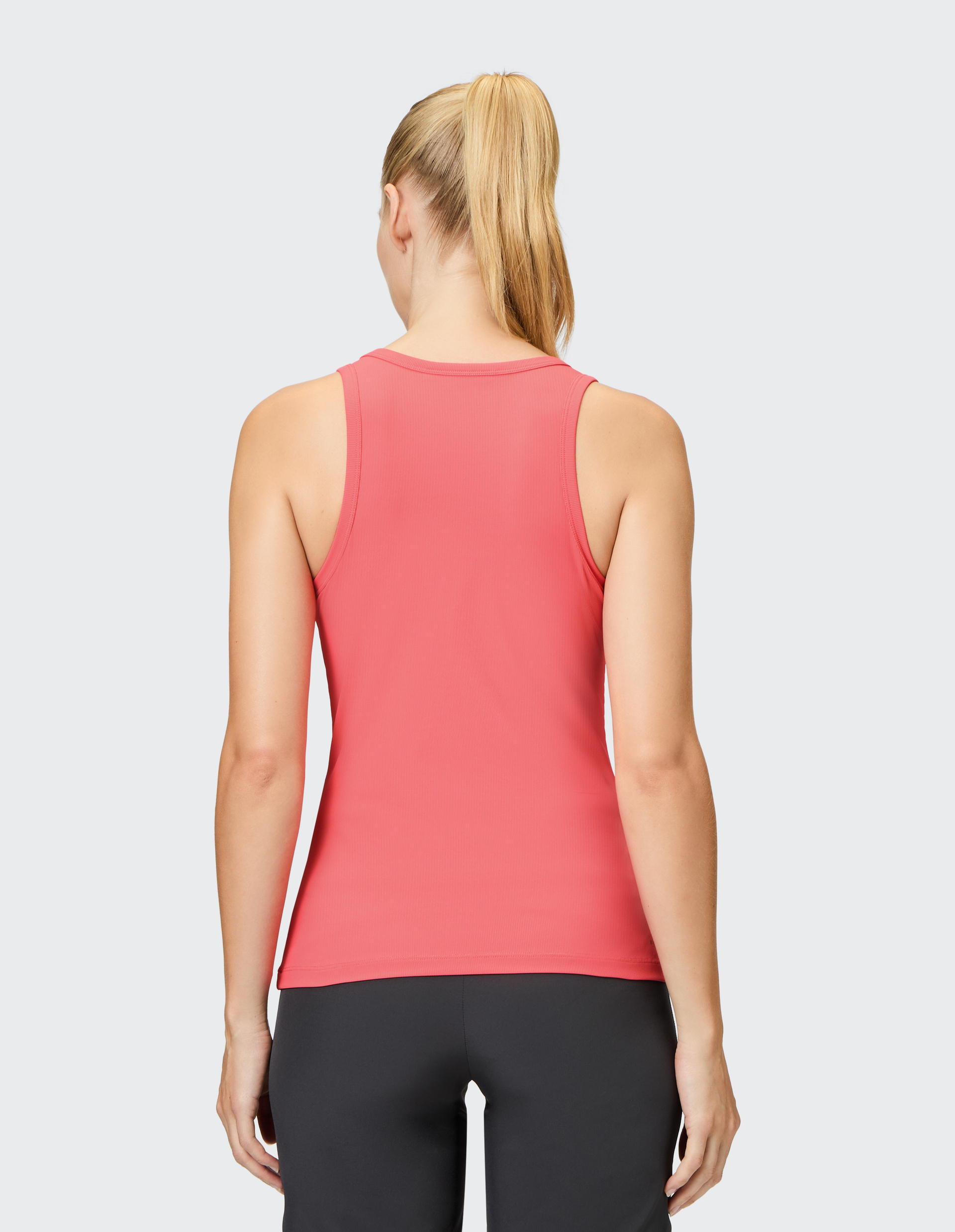 Frau mit blondem Pferdeschwanz trägt ein rotes ärmelloses Top und schwarze Hose, fotografiert von hinten auf grauem Hintergrund.